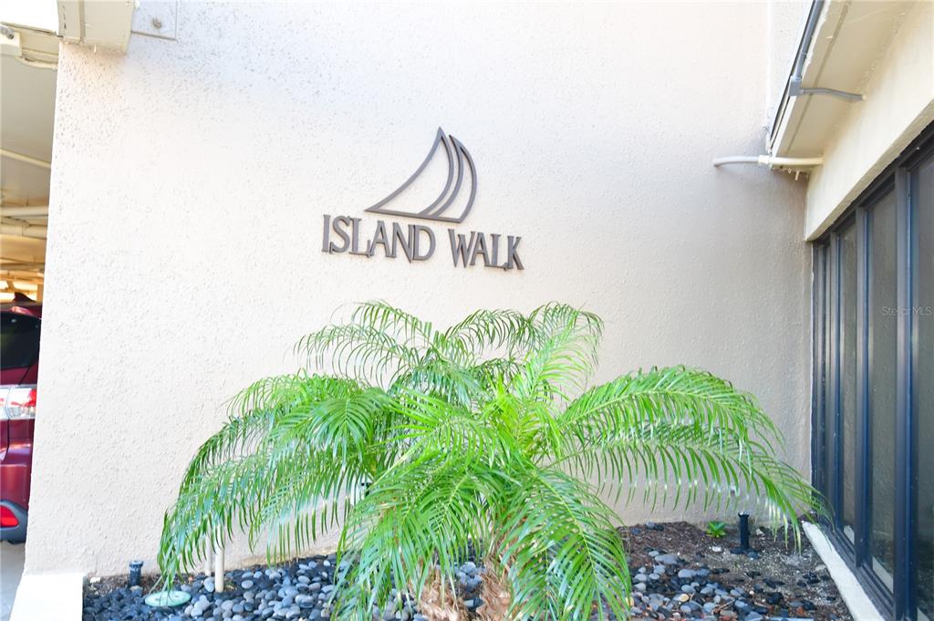 A palm tree sits in front of a wall featuring the Island Walk sign — 690 ISLAND WAY UNIT 208, CLEARWATER, FL