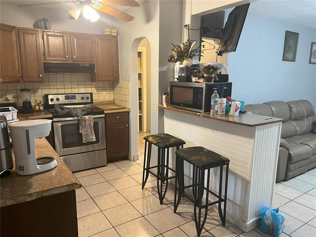 A kitchen features wooden cabinets, stainless steel appliances, a breakfast bar with stools, and tile flooring — 120 S SAN REMO AVENUE, CLEARWATER, FL