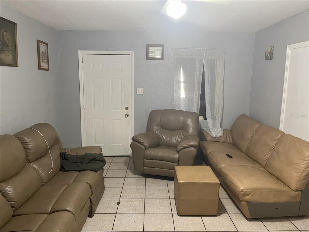 A living room features light gray walls, tiled flooring, and three pieces of tan leather furniture — 120 S SAN REMO AVENUE, CLEARWATER, FL