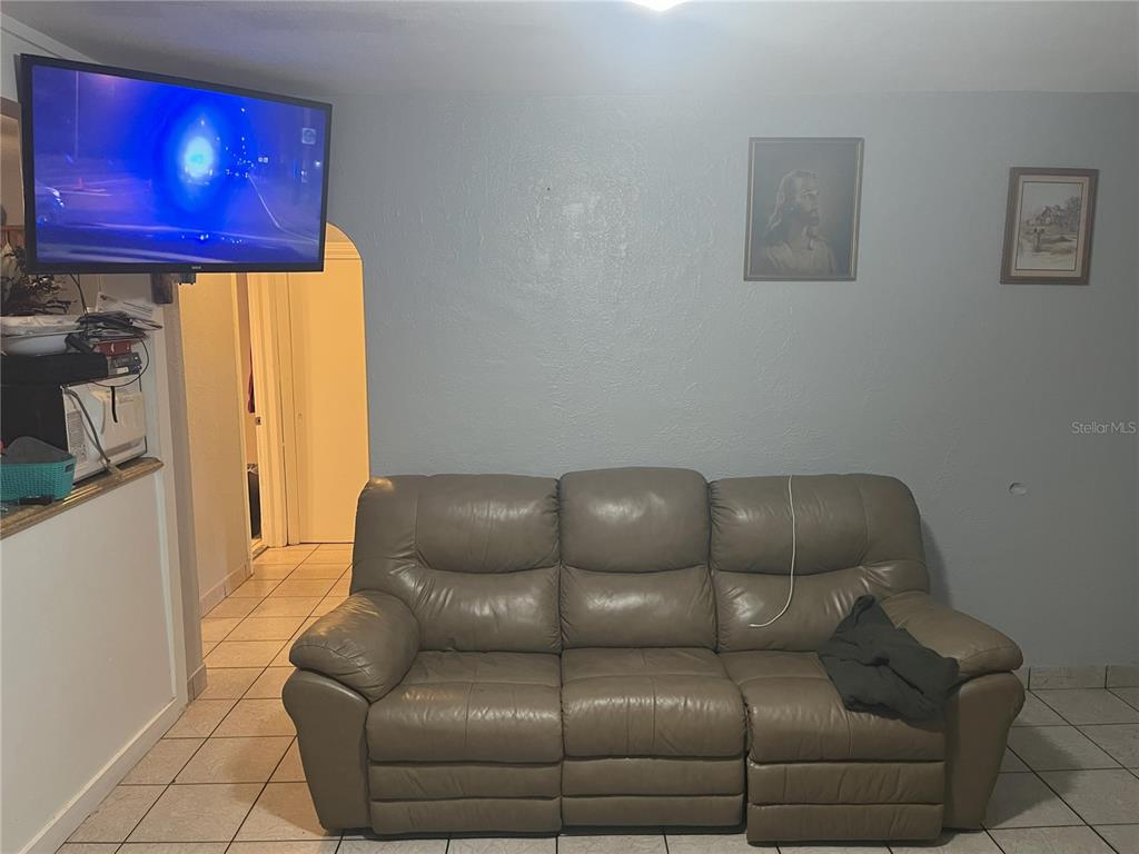 A living room features a tan leather sofa, a wall-mounted television, and two framed pictures — 120 S SAN REMO AVENUE, CLEARWATER, FL