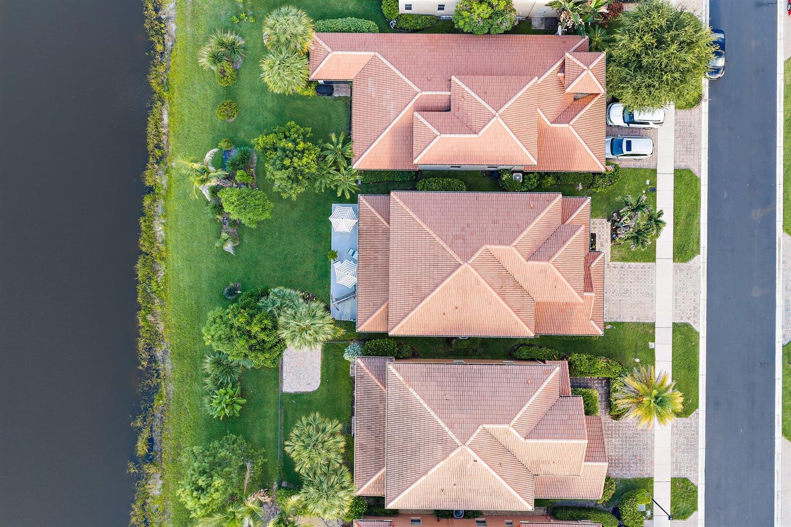 An aerial view shows three houses with tiled roofs, backyards, and a canal — 7835 SE Heritage Boulevard, Hobe Sound FL 33455, HOBE SOUND, FL