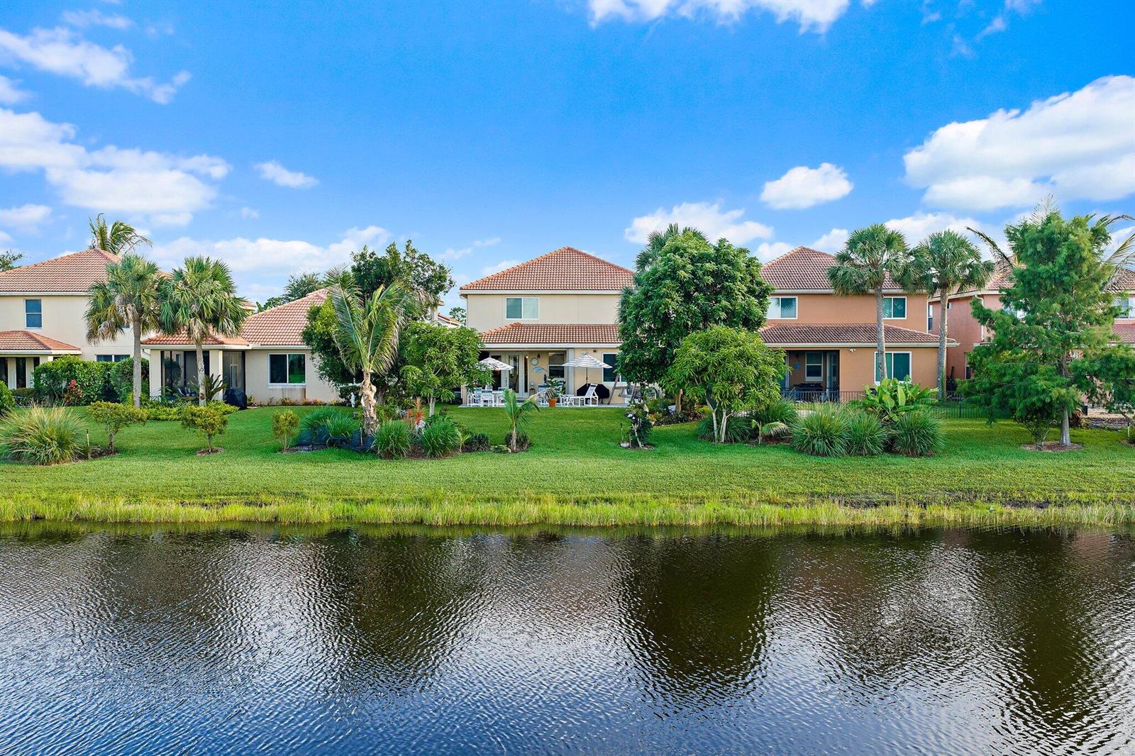 A row of residential houses with tile roofs sits behind a grassy lawn and pond — 7835 SE Heritage Boulevard, Hobe Sound FL 33455, HOBE SOUND, FL