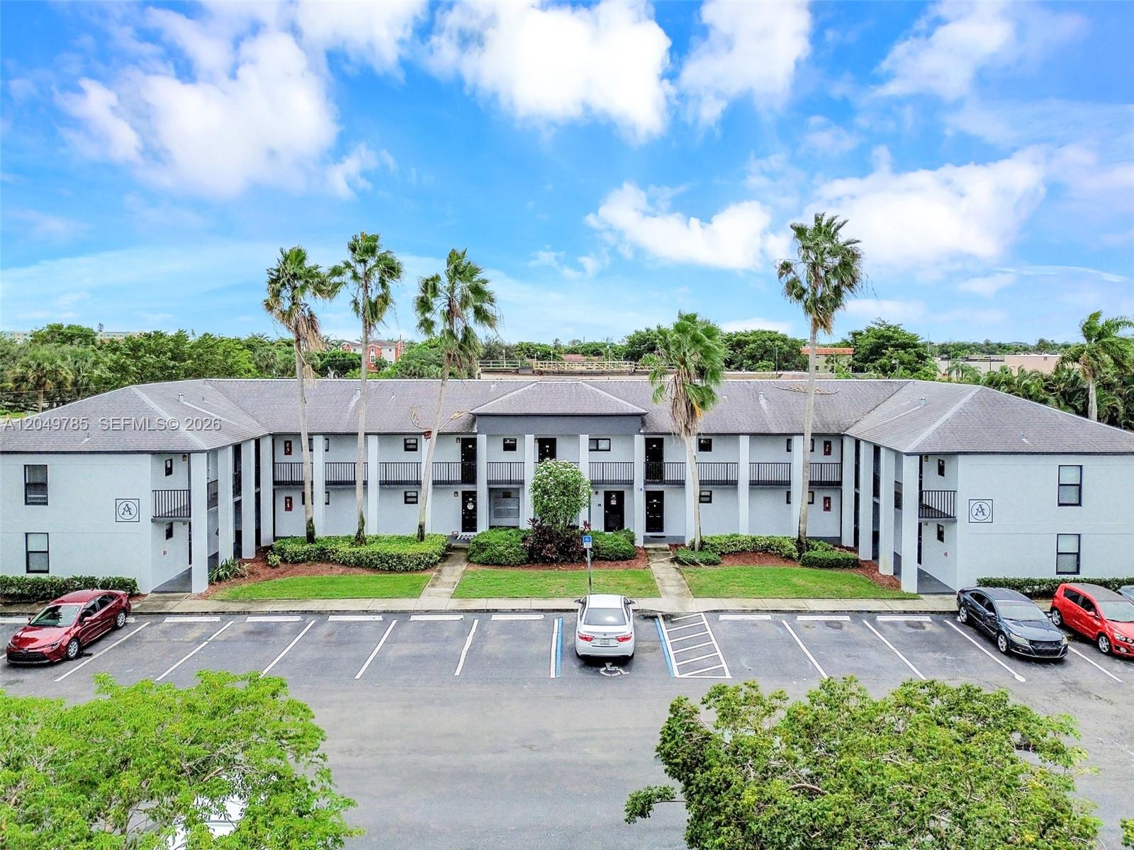 An exterior view of a two-story apartment building with palm trees and a parking lot — 7550 Stirling Rd # C203, Davie FL 33024, DAVIE, FL