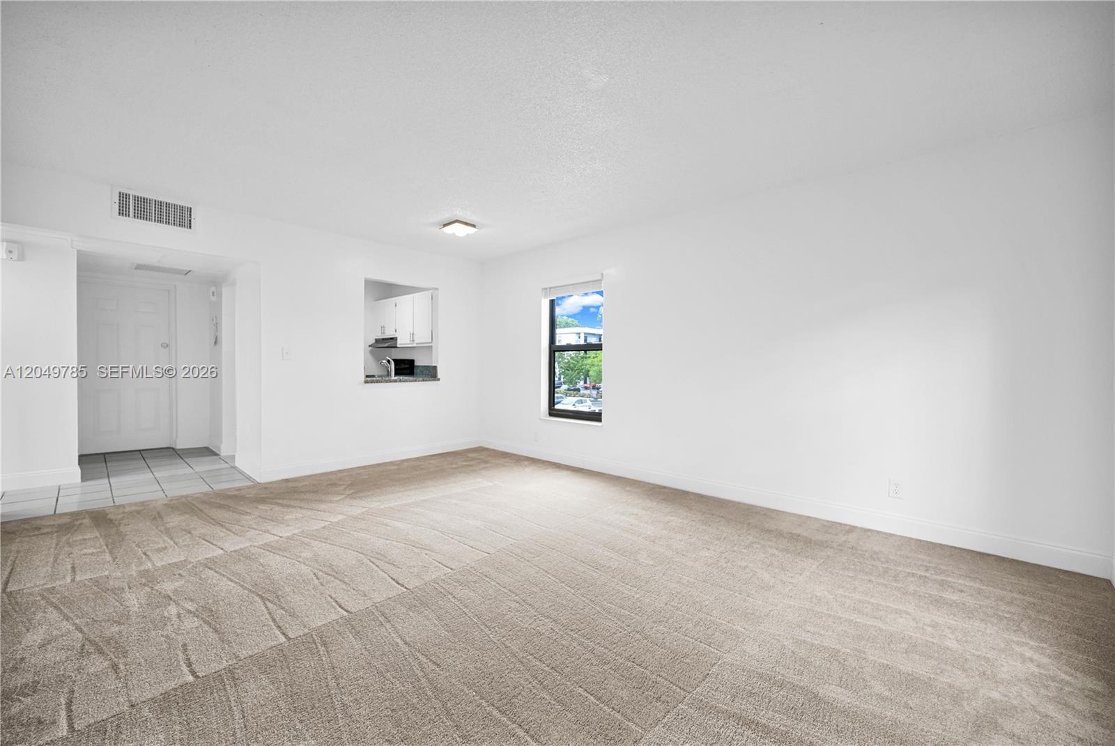 This living room features beige carpeting, white walls, and a window overlooking a parking lot — 7550 Stirling Rd # C203, Davie FL 33024, DAVIE, FL