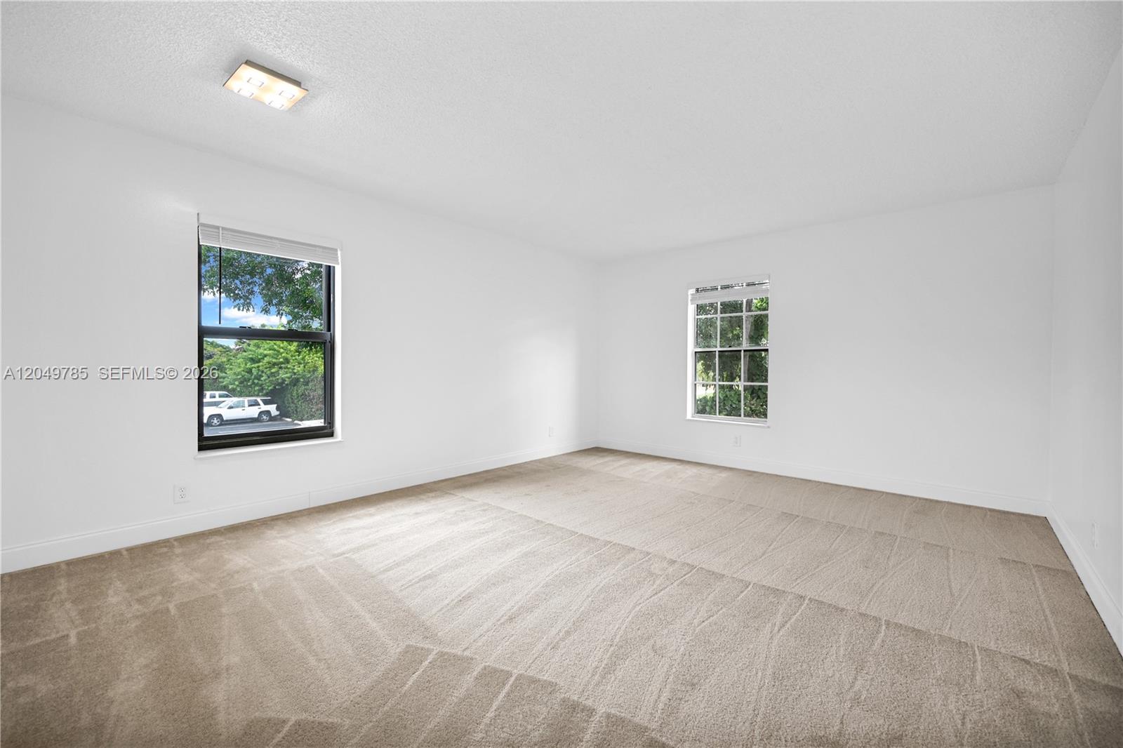 An empty bedroom features white walls, beige carpeting, two windows, and a ceiling light fixture — 7550 Stirling Rd # C203, Davie FL 33024, DAVIE, FL