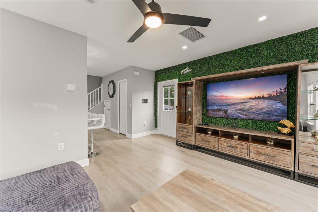 A living room features light wood flooring, a green wall accent, and a large television — 2951 KINGS ROAD, SANFORD, FL