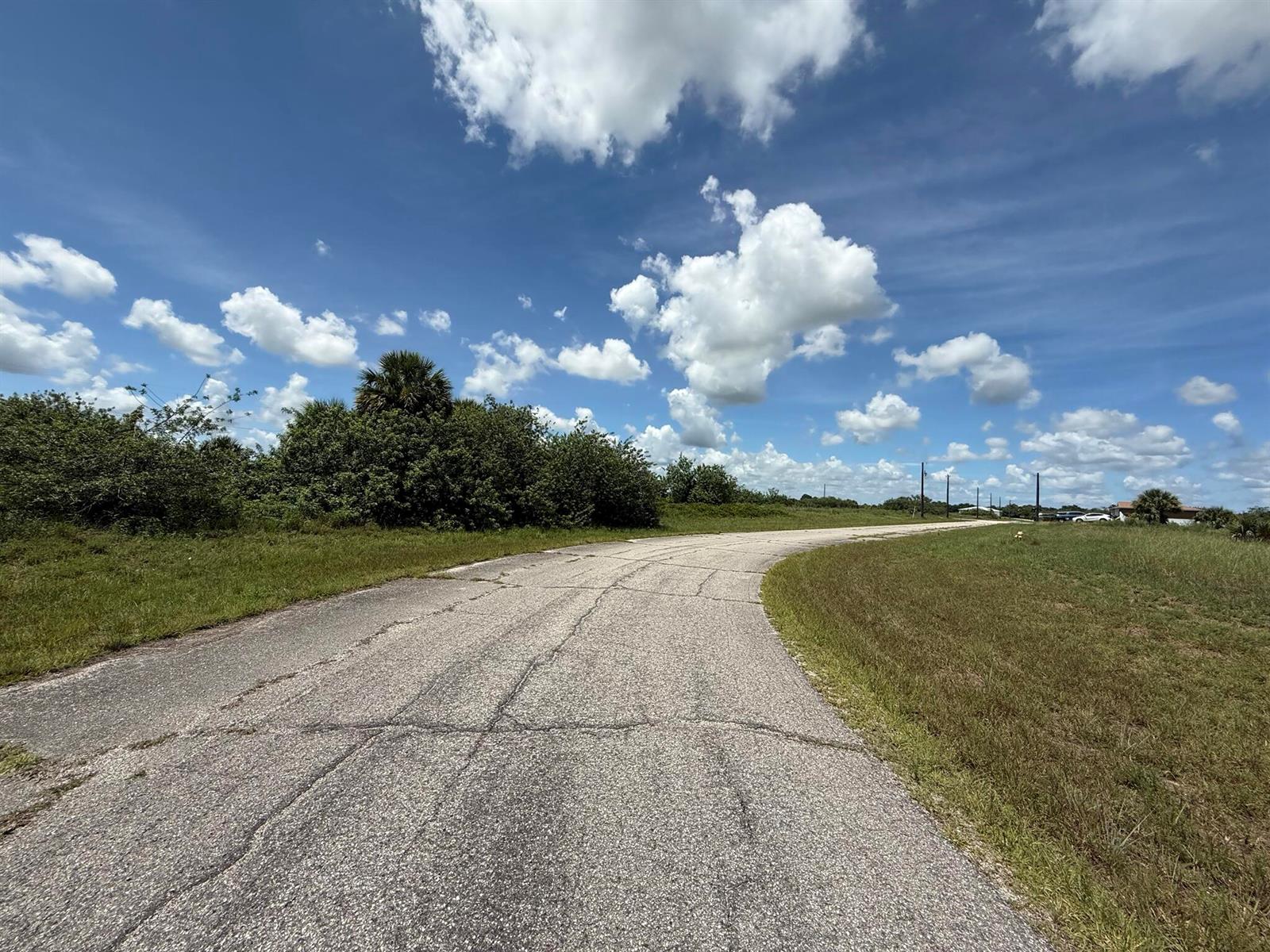 A paved road curves through a grassy field under a blue sky with scattered clouds — 113 Liberty Terrace, FL 33935, FL