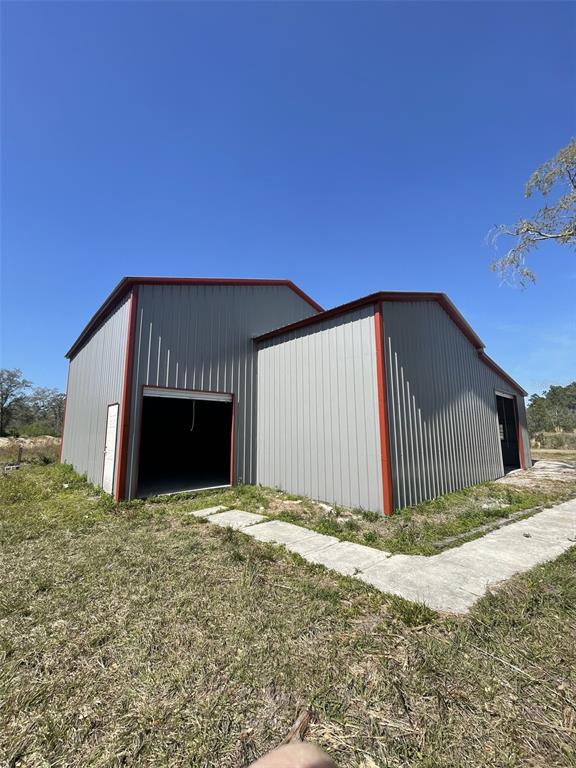 A metal-sided building with two garage bays and red trim sits on a grassy lot — 19100 COUNTY ROAD 33, GROVELAND, FL