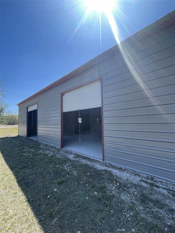 A metal-sided storage building with two open roll-up doors sits on a grassy lot — 19100 COUNTY ROAD 33, GROVELAND, FL