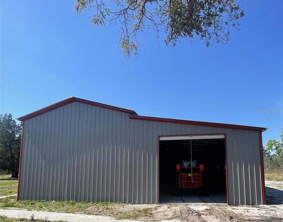A metal-sided barn with a red trim and an open bay housing a tractor — 19100 COUNTY ROAD 33, GROVELAND, FL