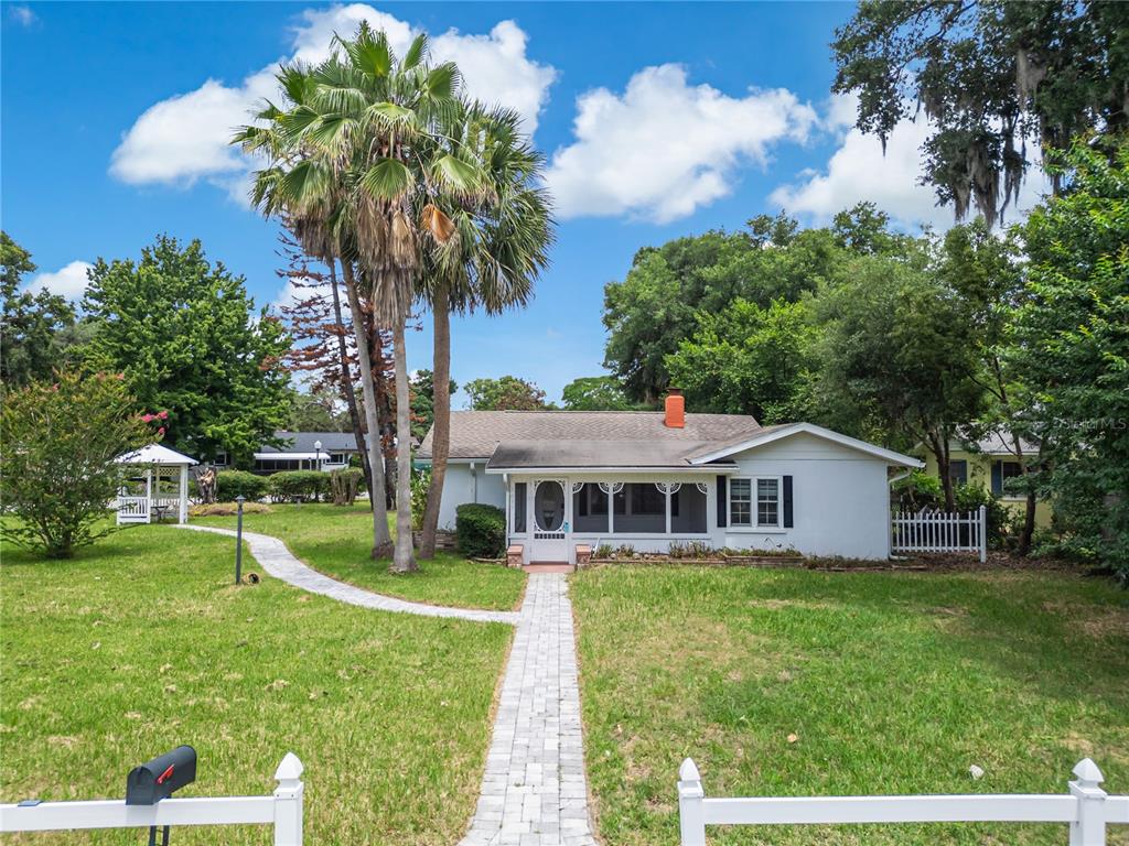 A white single-story house with a screened front porch sits behind a paved walkway — 1635 GERTRUDE PLACE, MOUNT DORA, FL