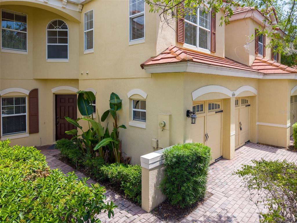 A two-story yellow stucco townhouse features a brown front door, garage, and paver driveway — 6959 SORRENTO STREET, ORLANDO, FL