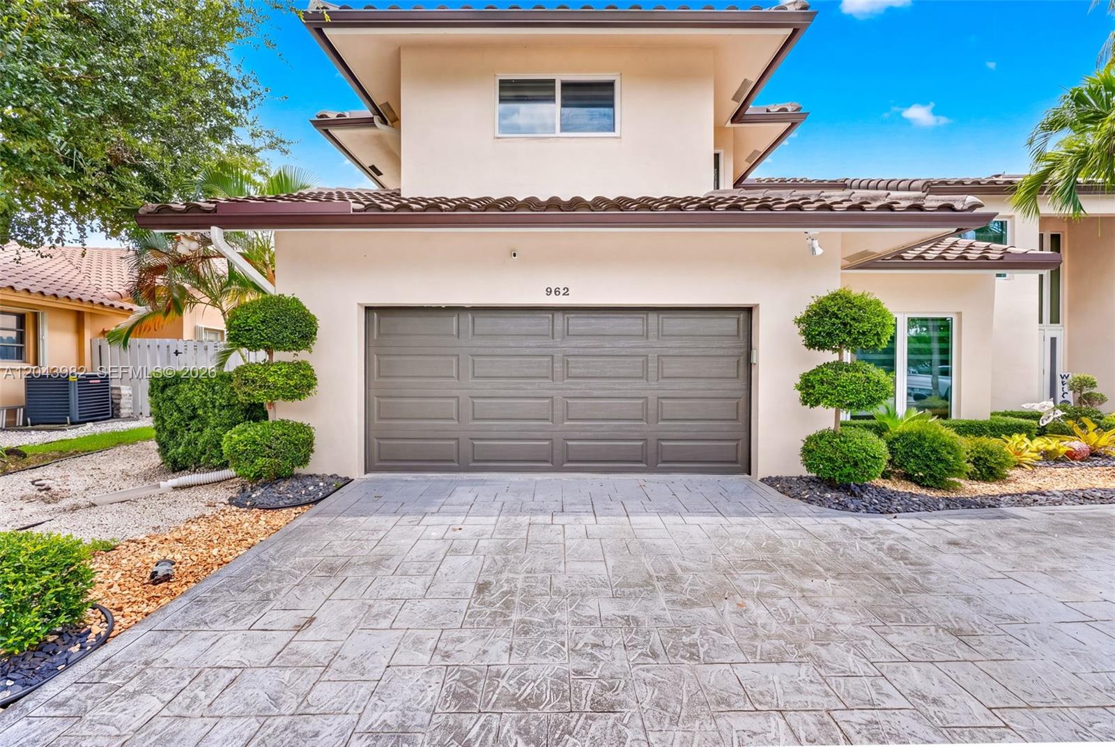 A two-story house exterior features a gray garage door, paved driveway, and manicured topiary trees — 962 SW 93rd Ter, Plantation FL 33324, PLANTATION, FL