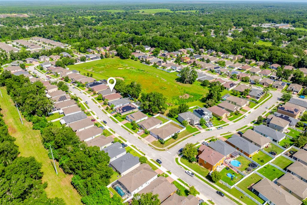 An aerial view shows a suburban neighborhood with houses, streets, and a large grassy field — 233 W FIESTA KEY LOOP, DELAND, FL