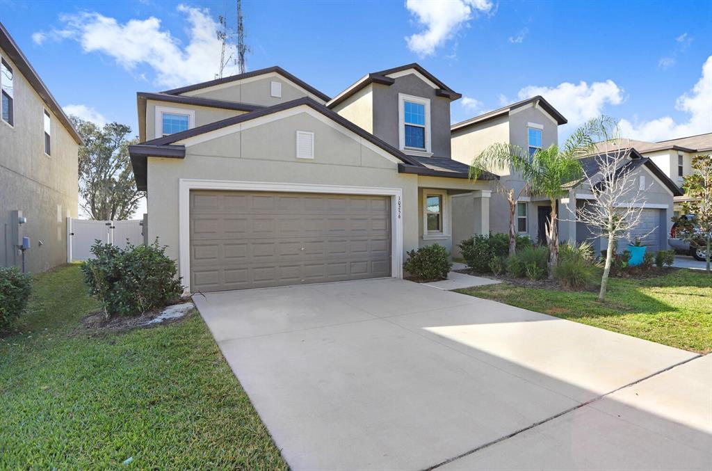 A two-story suburban house features a beige stucco exterior, a two-car garage, and a driveway — 10256 CARLOWAY HILLS DRIVE, WIMAUMA, FL