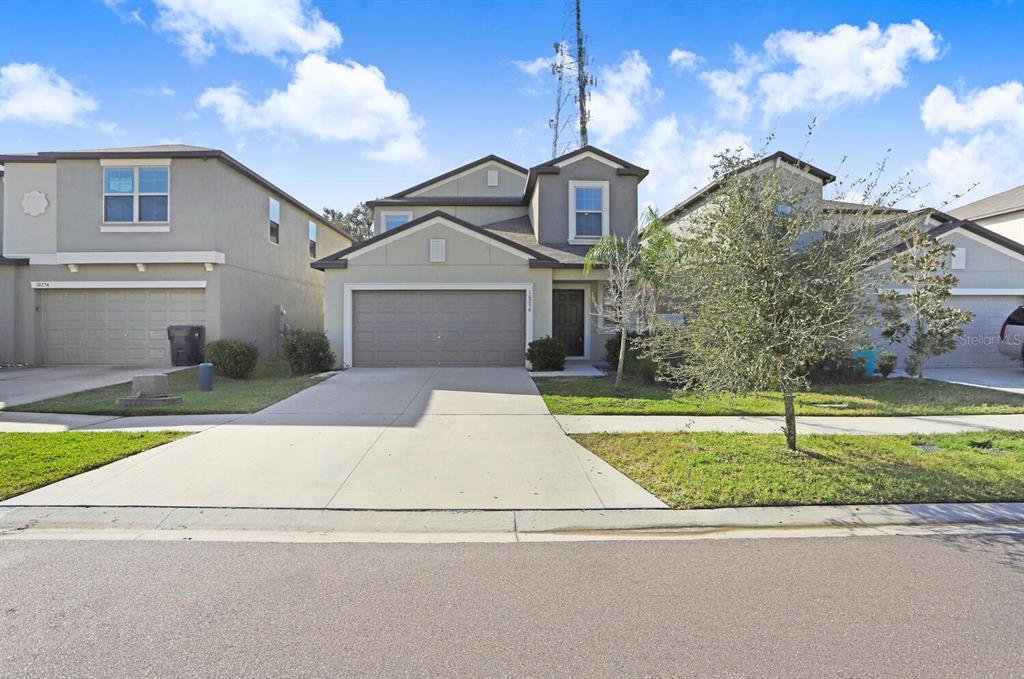 A two-story suburban house with a tan stucco exterior, a two-car garage, and a driveway — 10256 CARLOWAY HILLS DRIVE, WIMAUMA, FL