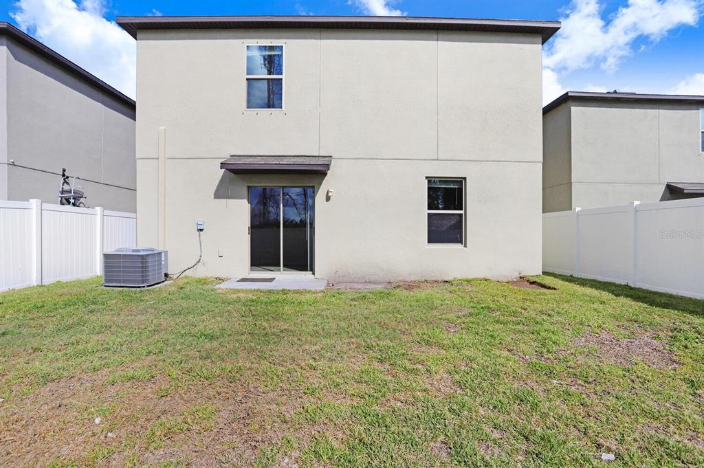 The exterior rear view of a two-story house features a sliding glass door and yard — 10256 CARLOWAY HILLS DRIVE, WIMAUMA, FL