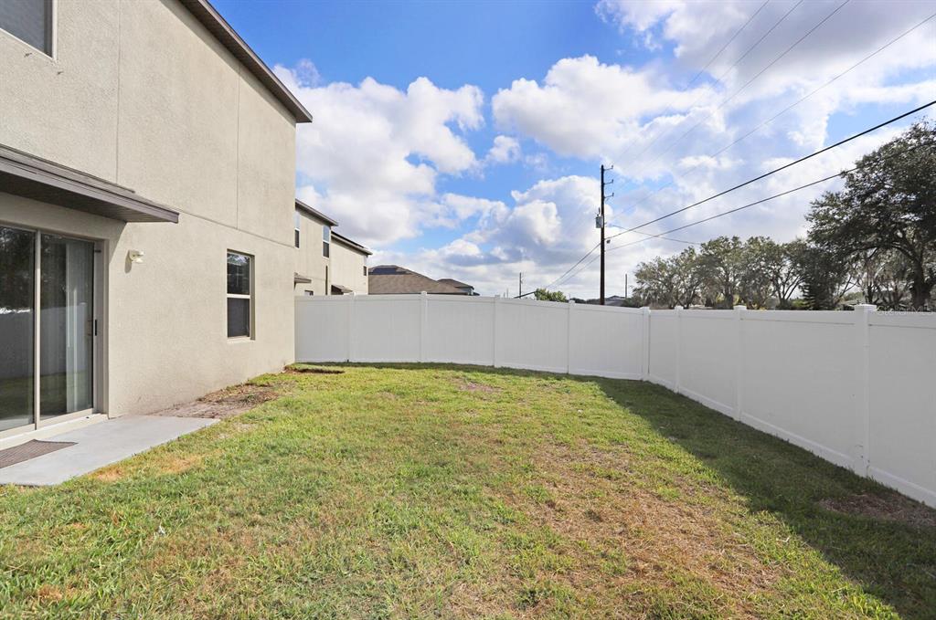A backyard with a grass lawn, a concrete patio, and a white vinyl privacy fence — 10256 CARLOWAY HILLS DRIVE, WIMAUMA, FL