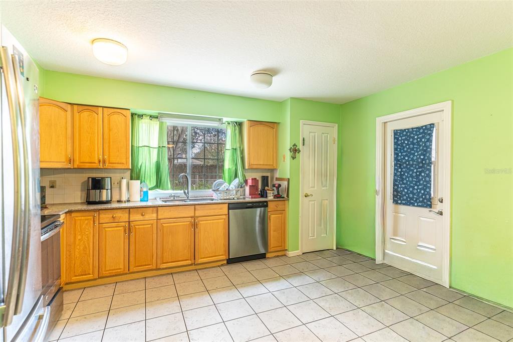 A kitchen with light green walls, wooden cabinets, stainless steel appliances, and tiled flooring — 5103 GREENBROOK LANE, LAKELAND, FL