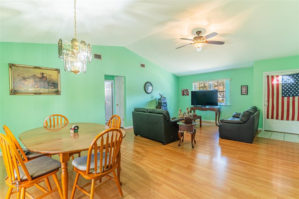 A living and dining area with light green walls, wood flooring, and a vaulted ceiling — 5103 GREENBROOK LANE, LAKELAND, FL