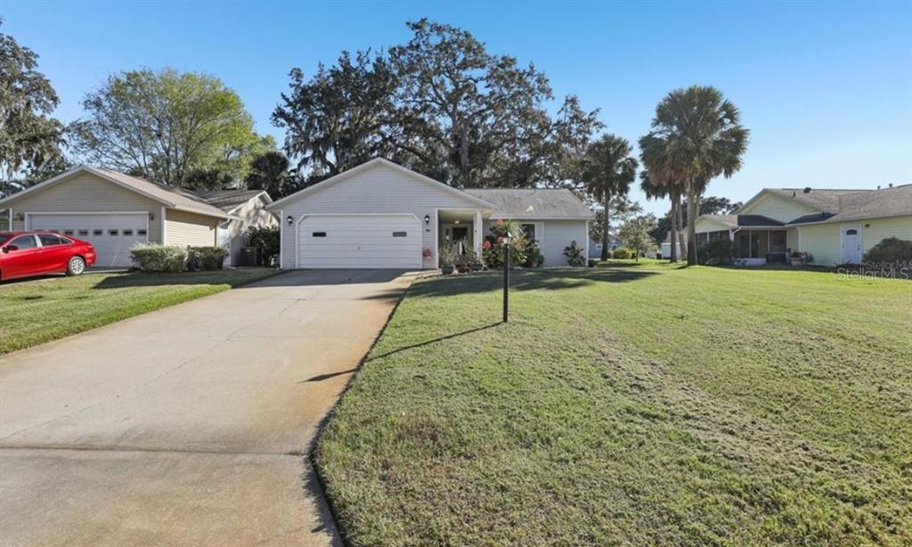 A single-story house with a white garage, a concrete driveway, and a large front lawn — 304 BRIGADOON CIRCLE, LEESBURG, FL