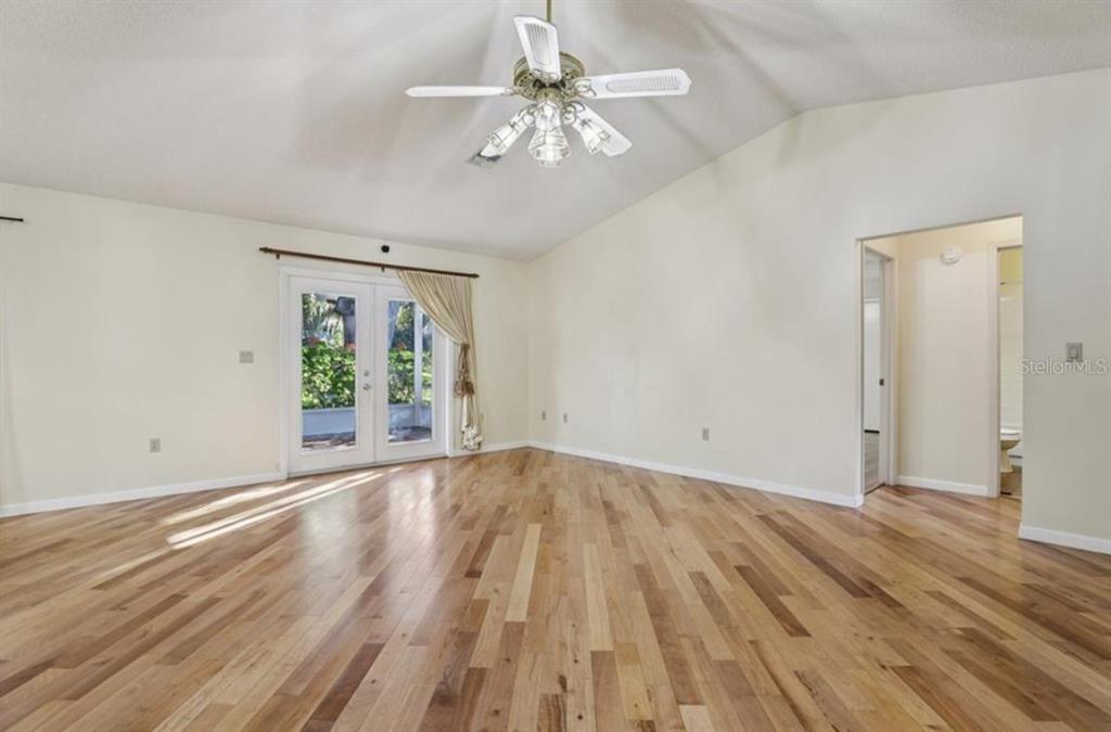 An empty room with hardwood floors, a vaulted ceiling, a ceiling fan, and glass doors — 304 BRIGADOON CIRCLE, LEESBURG, FL