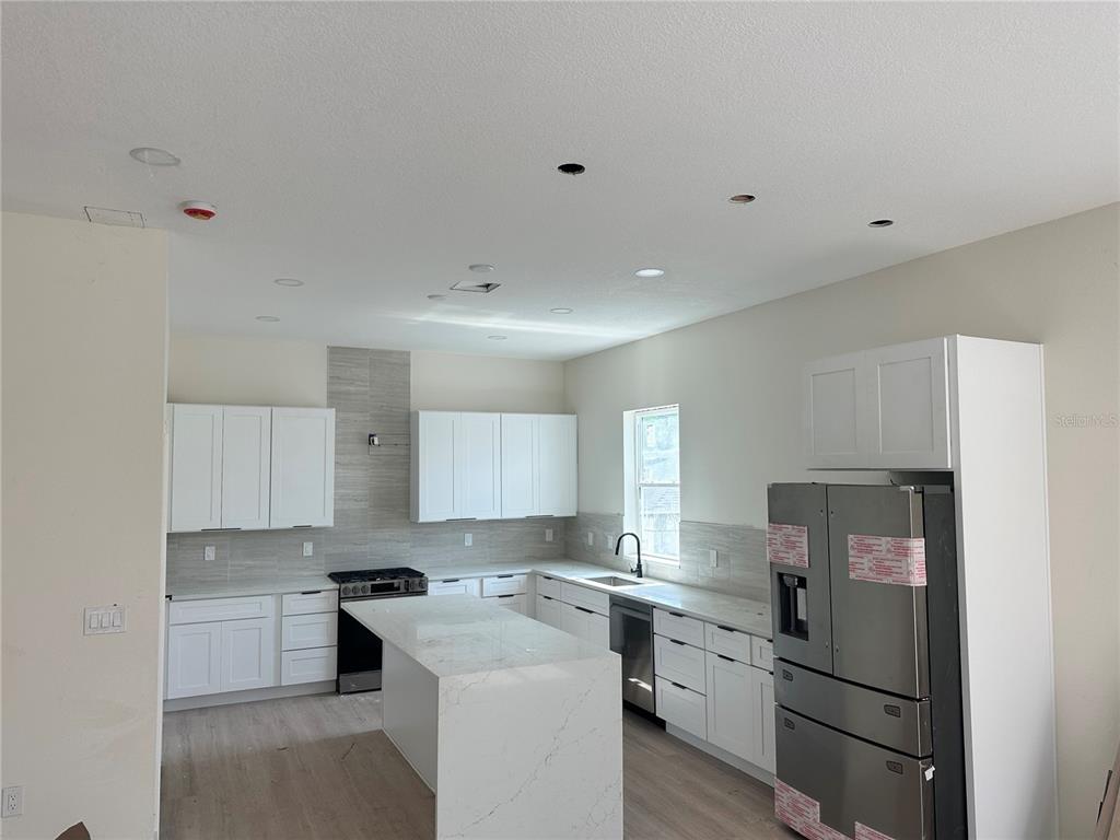 A modern kitchen features white cabinetry, a marble-topped island, stainless steel appliances, and tiled backsplashes — 2142 5TH AVENUE N, ST PETERSBURG, FL