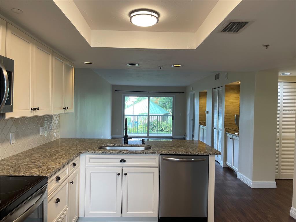 A kitchen with white cabinets, granite countertops, and a stainless steel dishwasher overlooks a balcony — 2320 TERRA CEIA BAY BOULEVARD UNIT 203, PALMETTO, FL