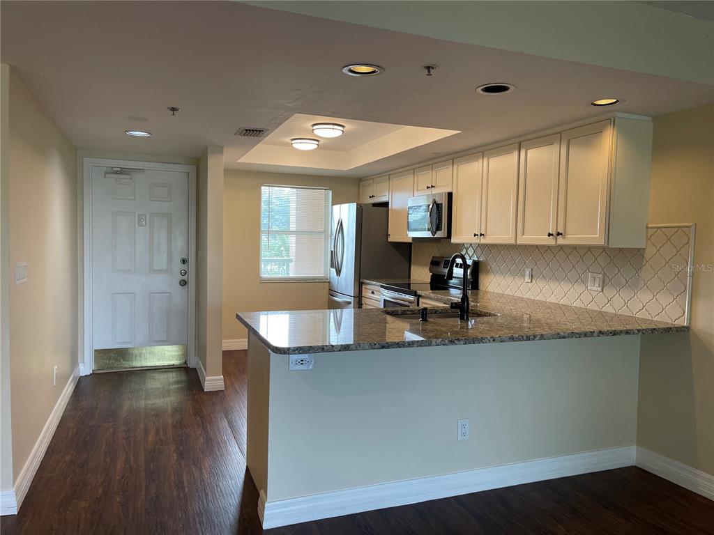 A kitchen features white cabinets, granite countertops, a stainless steel refrigerator, and dark wood flooring — 2320 TERRA CEIA BAY BOULEVARD UNIT 203, PALMETTO, FL