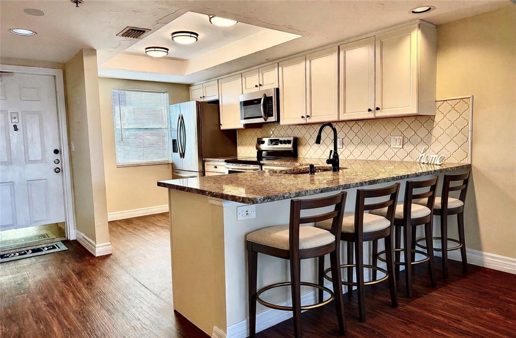 A kitchen features white cabinets, granite countertops, a breakfast bar with four stools, and stainless appliances — 2320 TERRA CEIA BAY BOULEVARD UNIT 203, PALMETTO, FL