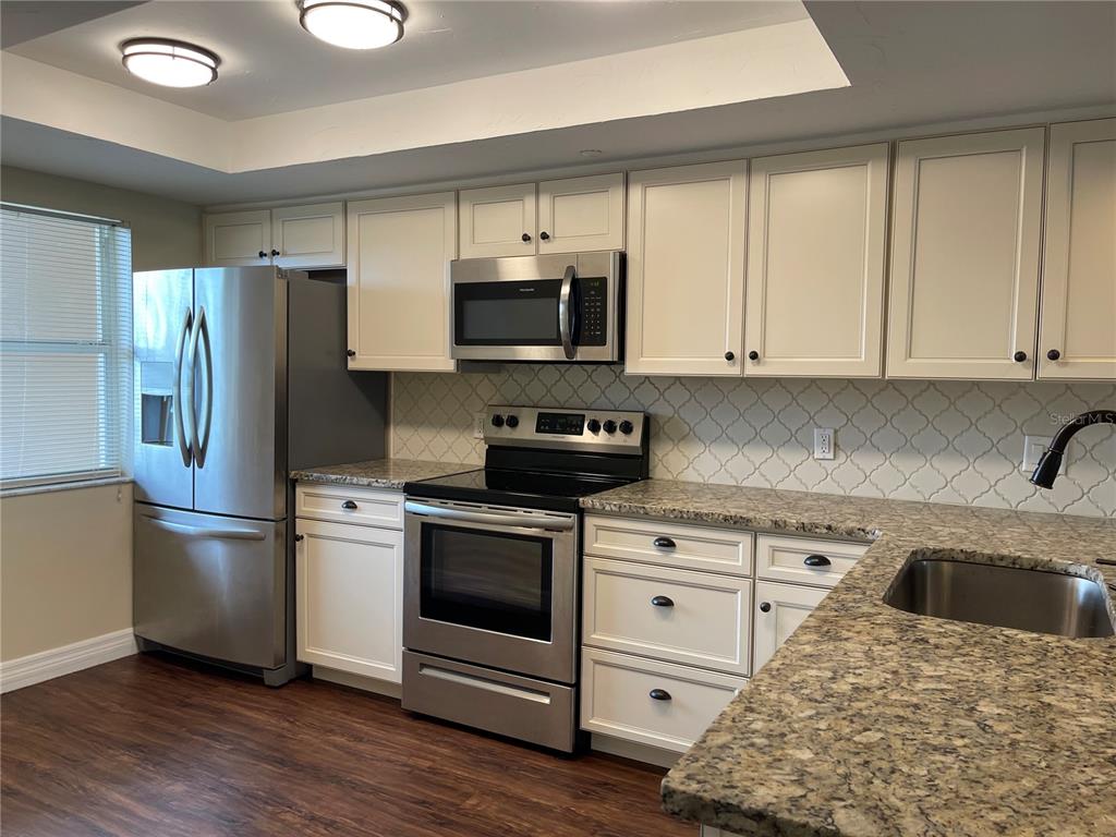 A kitchen features stainless steel appliances, white cabinets, granite countertops, and a patterned tile backsplash — 2320 TERRA CEIA BAY BOULEVARD UNIT 203, PALMETTO, FL