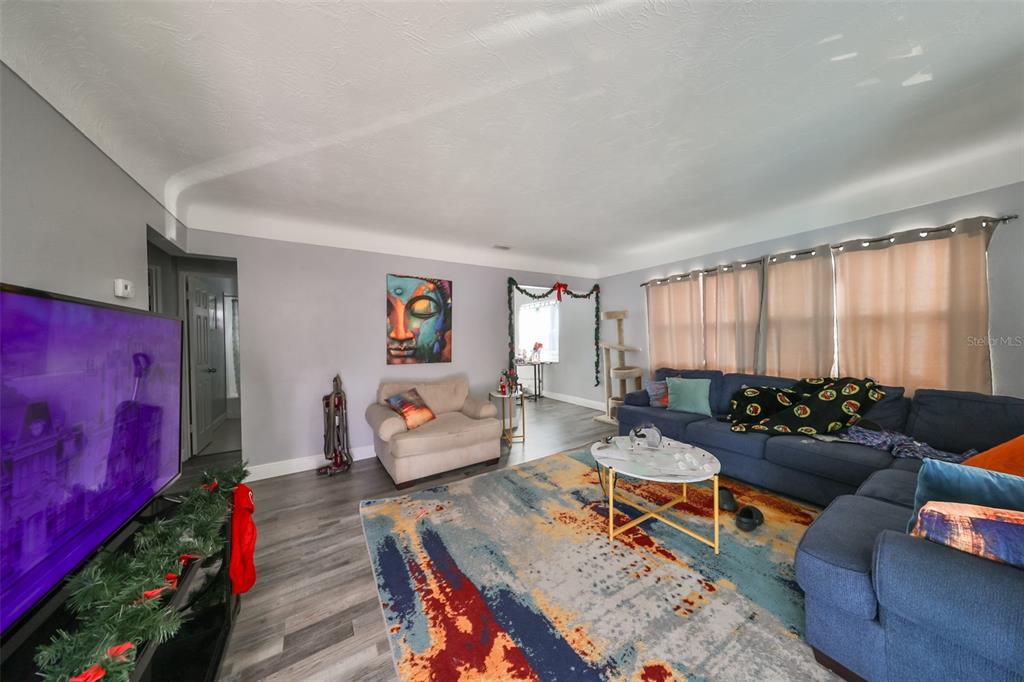 A living room features gray walls, wood-look flooring, a blue sectional sofa, and a colorful rug — 5117 12TH AVE S, GULFPORT, FL UNIT 33707, GULFPORT, FL
