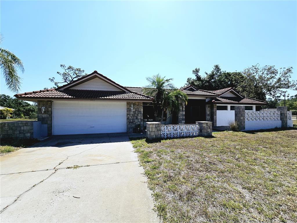 A single-story house with a white garage door, stone accents, and a decorative concrete wall — 2411 BELLE ROAD, ENGLEWOOD, FL