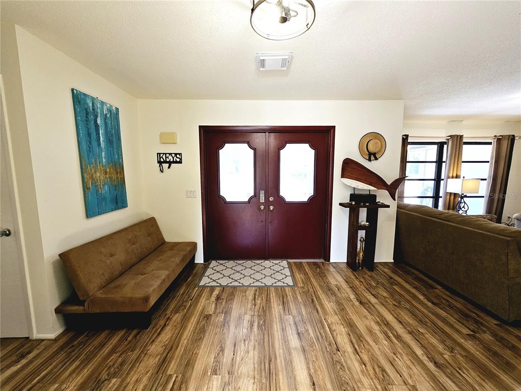 An entryway features wood-look flooring, a brown bench, and double front doors — 2411 BELLE ROAD, ENGLEWOOD, FL