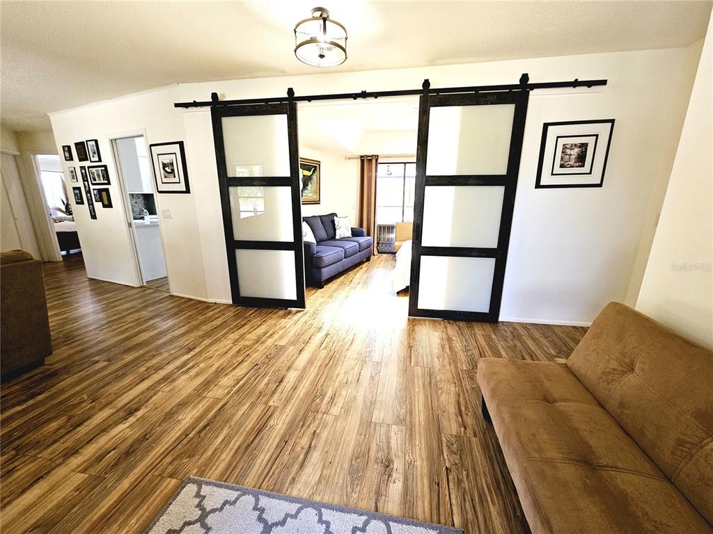A living room features wood-look flooring, a tan sofa, and sliding barn doors to another room — 2411 BELLE ROAD, ENGLEWOOD, FL