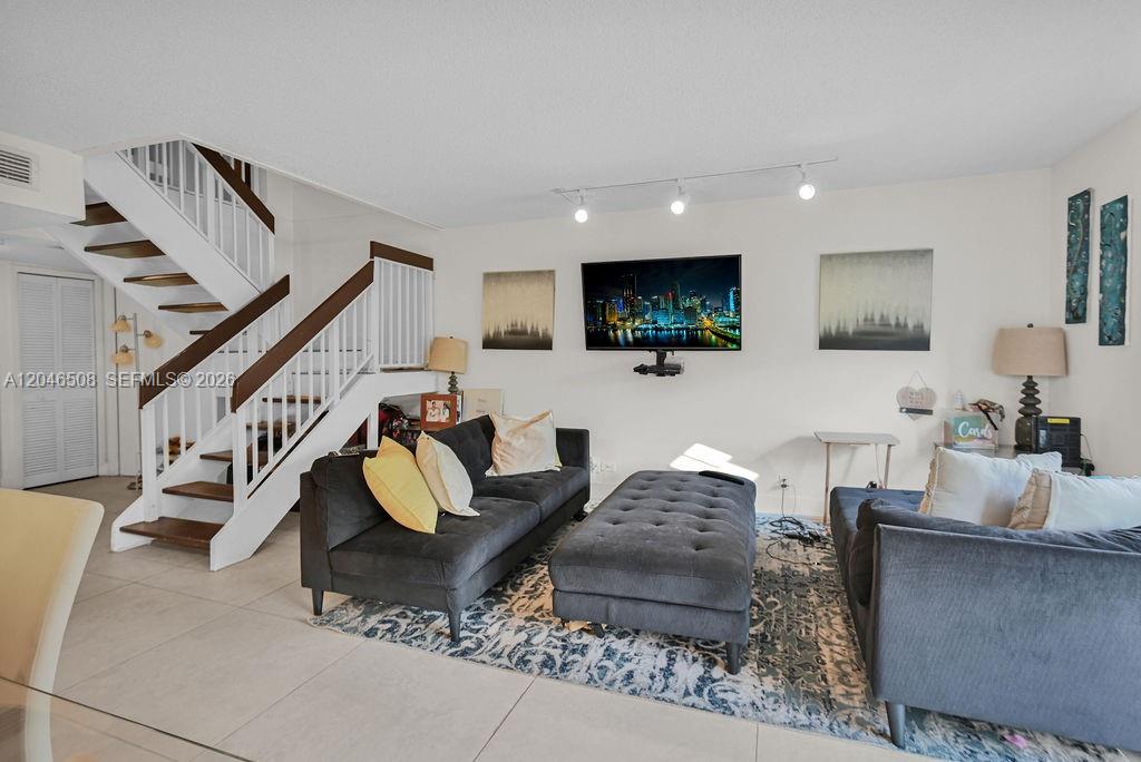 A living room features a dark sofa, a tufted ottoman, and a staircase with white railings — 7887 NW 7th Ct, Plantation FL 33324, PLANTATION, FL