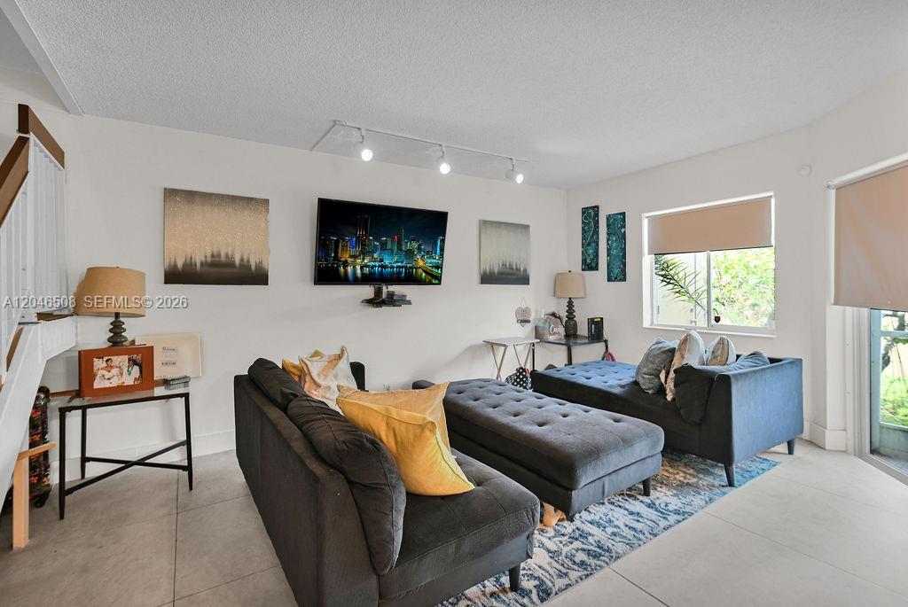 A living room features gray sofas, a central ottoman, a wall-mounted television, and tile flooring — 7887 NW 7th Ct, Plantation FL 33324, PLANTATION, FL