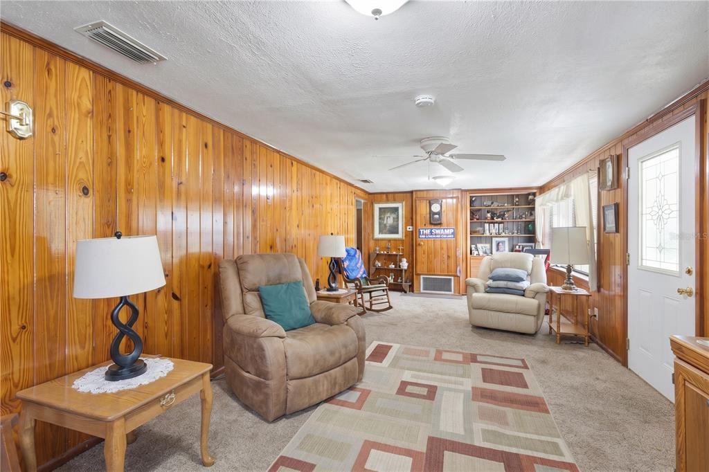 A living room features wood-paneled walls, carpeted flooring, a ceiling fan, and two armchairs — 604 W MARKET ROAD, STARKE, FL