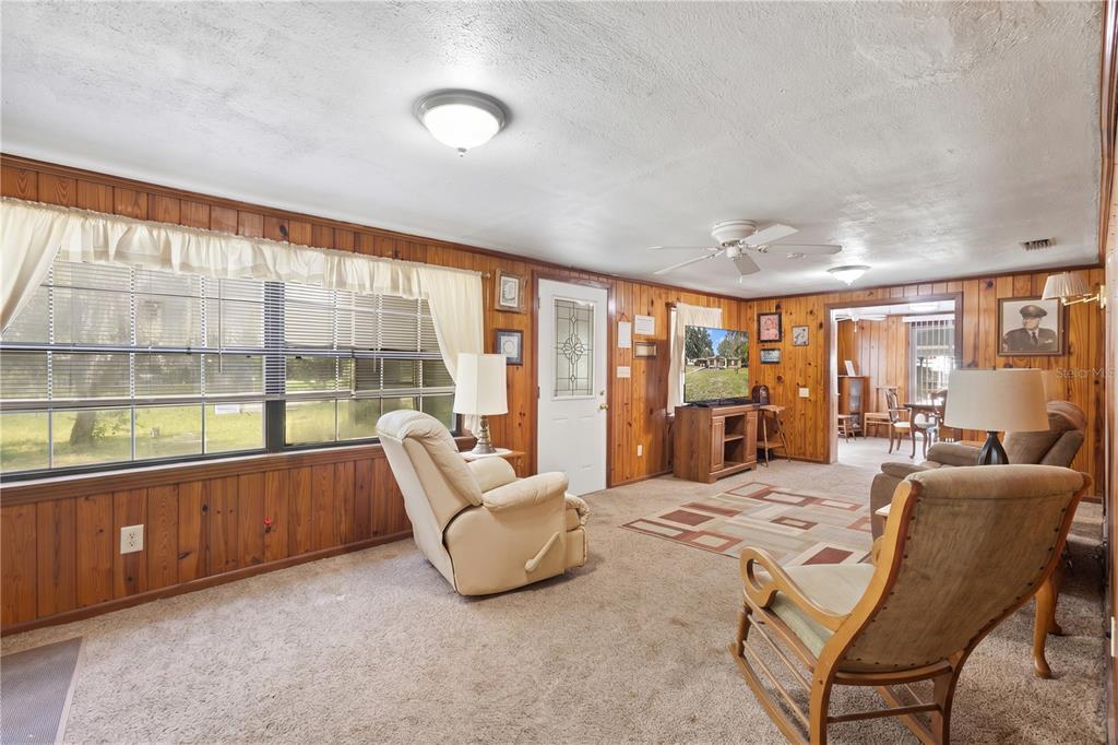 A living room features wood-paneled walls, beige carpeting, a ceiling fan, and a large window — 604 W MARKET ROAD, STARKE, FL