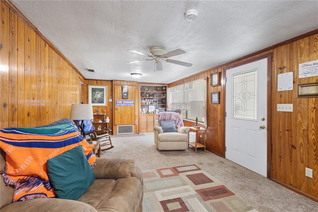 A living room features wood-paneled walls, a ceiling fan, carpeted flooring, and a white door — 604 W MARKET ROAD, STARKE, FL