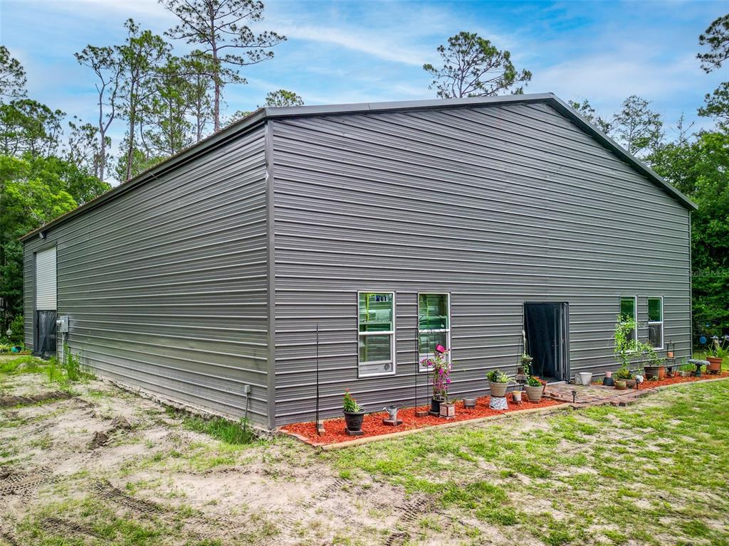 A large, gray metal-sided building with several windows and a door sits on a sandy lot — 425 WESTERN ROAD, NEW SMYRNA BEACH, FL
