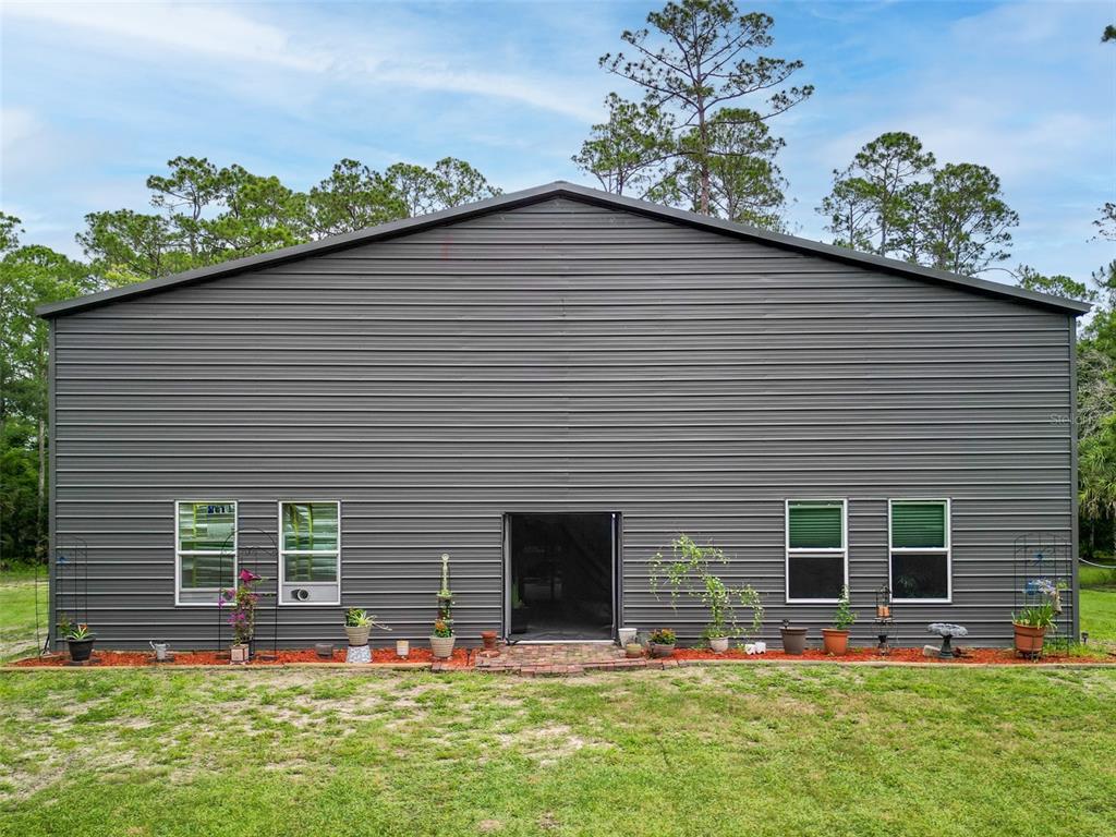 A dark gray metal-sided building with four windows and a central doorway sits on grass — 425 WESTERN ROAD, NEW SMYRNA BEACH, FL