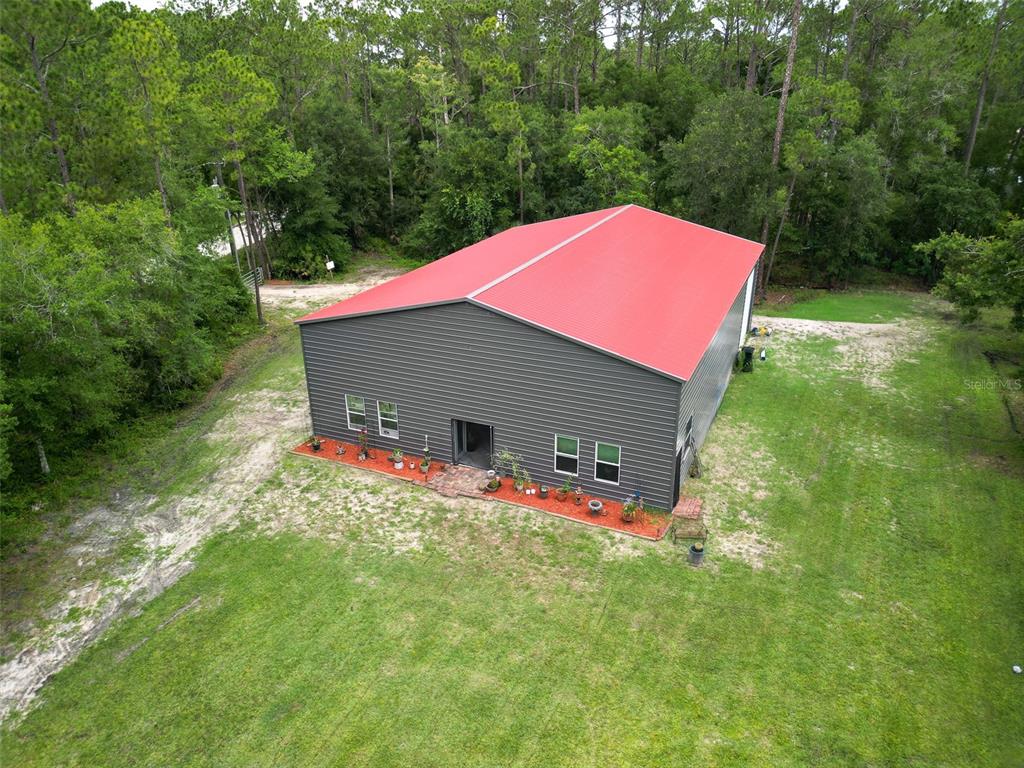 An aerial view shows a gray metal building with a red roof on a wooded lot — 425 WESTERN ROAD, NEW SMYRNA BEACH, FL
