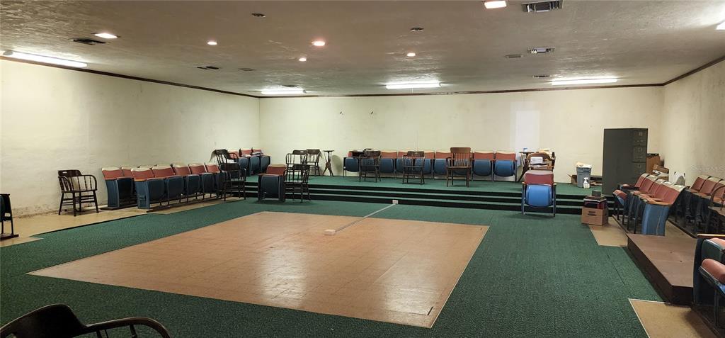 A large, carpeted room features a central wooden dance floor and tiered theater-style seating — 145 NW 257TH STREET, NEWBERRY, FL
