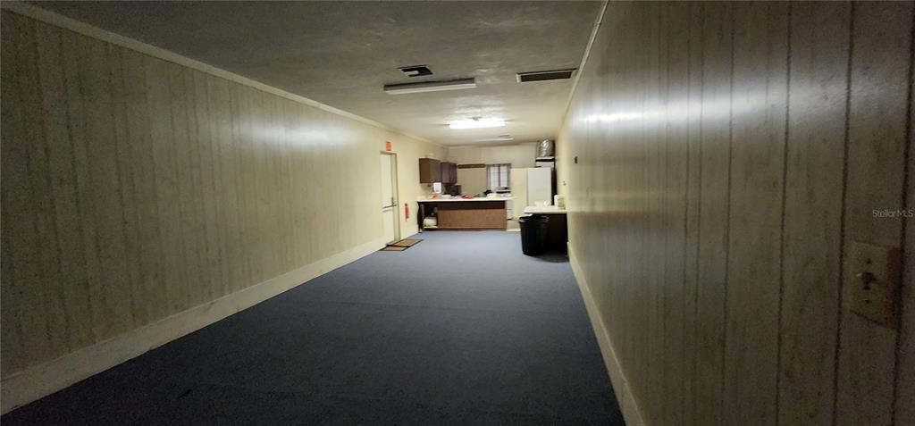 A long, narrow room features wood-paneled walls, blue carpeting, and a kitchen area in back — 145 NW 257TH STREET, NEWBERRY, FL