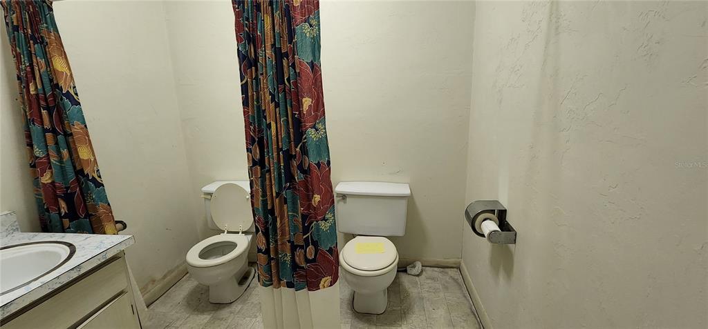 A bathroom features two toilets, a vanity with a sink, and floral patterned shower curtains — 145 NW 257TH STREET, NEWBERRY, FL