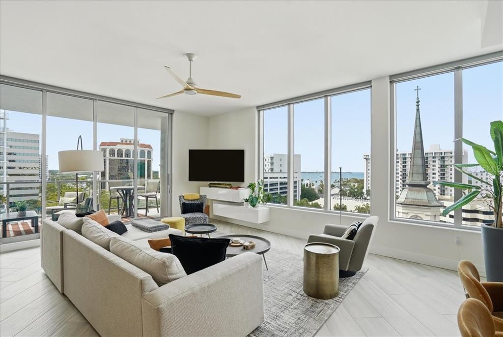 A modern living room features floor-to-ceiling windows with city and water views — 111 S PINEAPPLE AVENUE UNIT 714, SARASOTA, FL