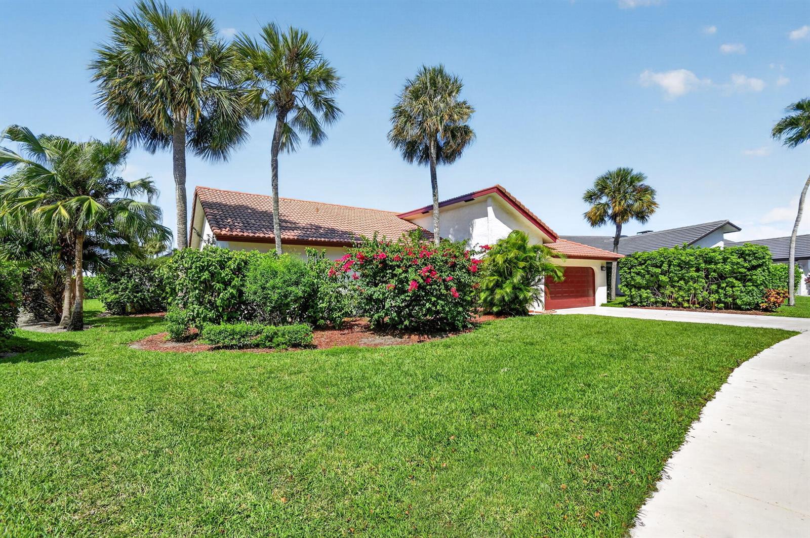A single-story house with a tile roof, red garage door, and lush landscaping — 2400 SW 23rd Cranbrook Drive, Boynton Beach FL 33436, BOYNTON BEACH, FL