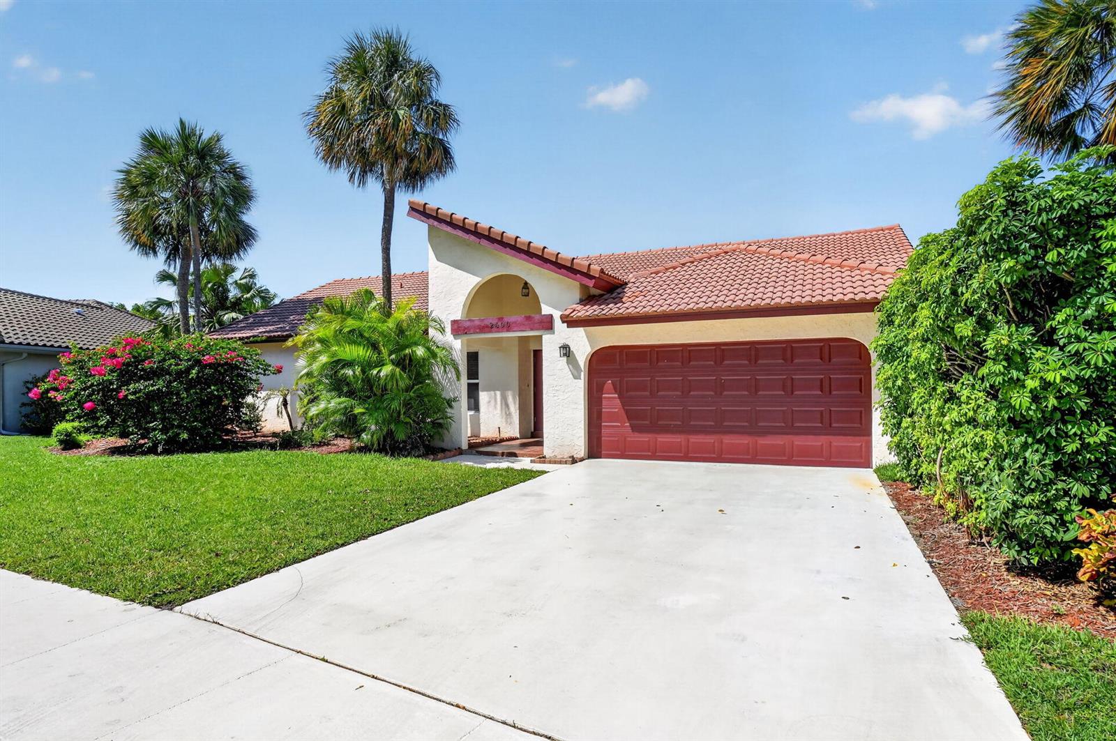 A single-story house with a red tile roof, white stucco exterior, and a red garage door — 2400 SW 23rd Cranbrook Drive, Boynton Beach FL 33436, BOYNTON BEACH, FL