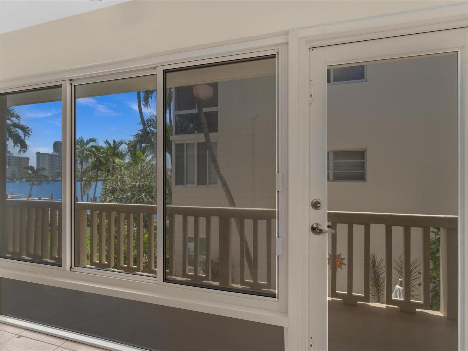 A view through a white-framed window and door looking out onto a balcony and water — 2000 Diana Drive # 207, Hallandale Beach FL 33009, HALLANDALE BEACH, FL